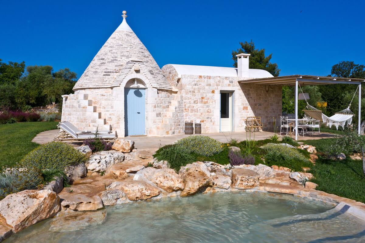 A stone building with a conical roof, a pool, and outdoor seating.