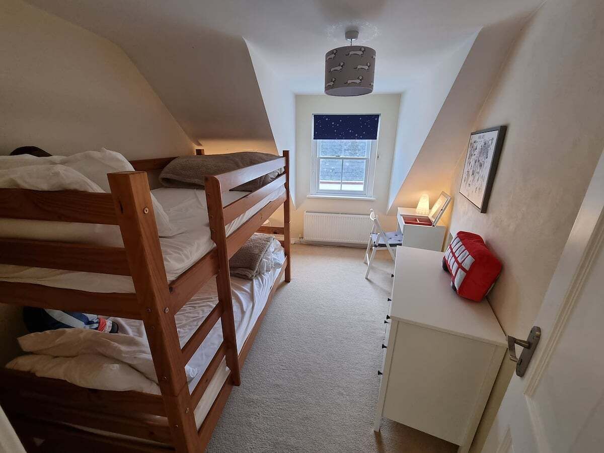 Ein Schlafsaalzimmer mit Etagenbetten, einem Schreibtisch, einem Heizkörper und einem Fenster mit Blick zum Himmel.
