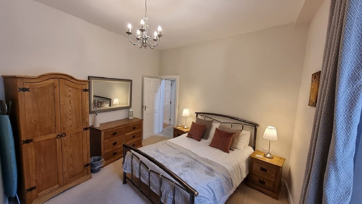 A bedroom with a bed, nightstands, a dresser, a mirror, and a chandelier.