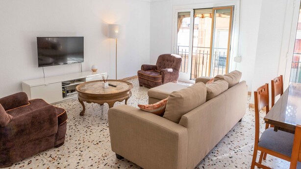 A living room with a sofa, armchairs, a TV, a coffee table, and a dining table with chairs.