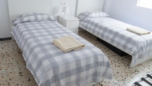 A room with two beds, each with a checkered bedspread and a folded towel on the bed. There is a nightstand with a lamp between the beds.