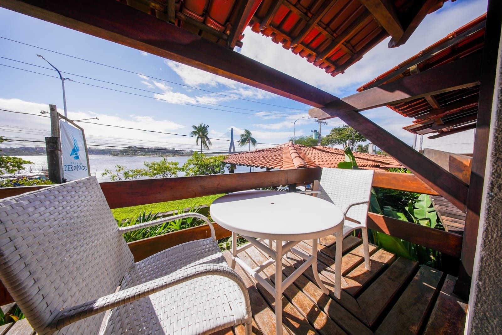 Un balcon avec des fauteuils en osier et une table, d’où l’on peut admirer un plan d’eau et des palmiers.