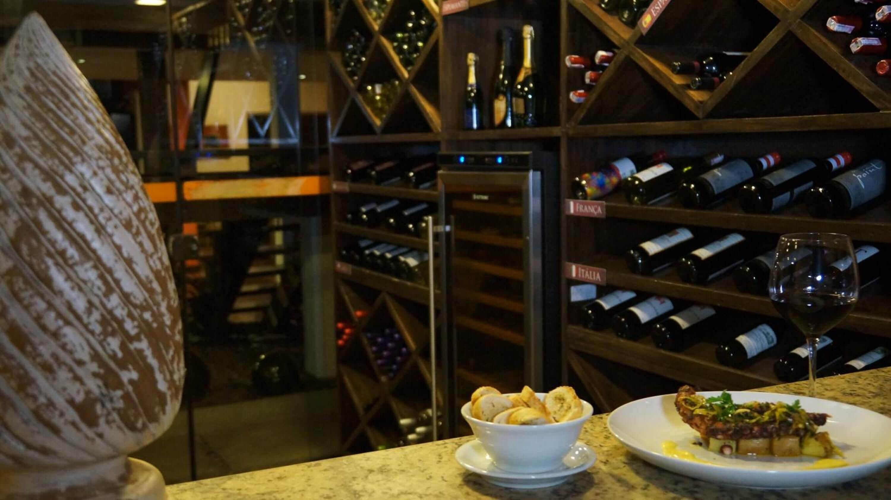 A wine cellar with shelves of wine bottles, a wine glass, and a plate of food.