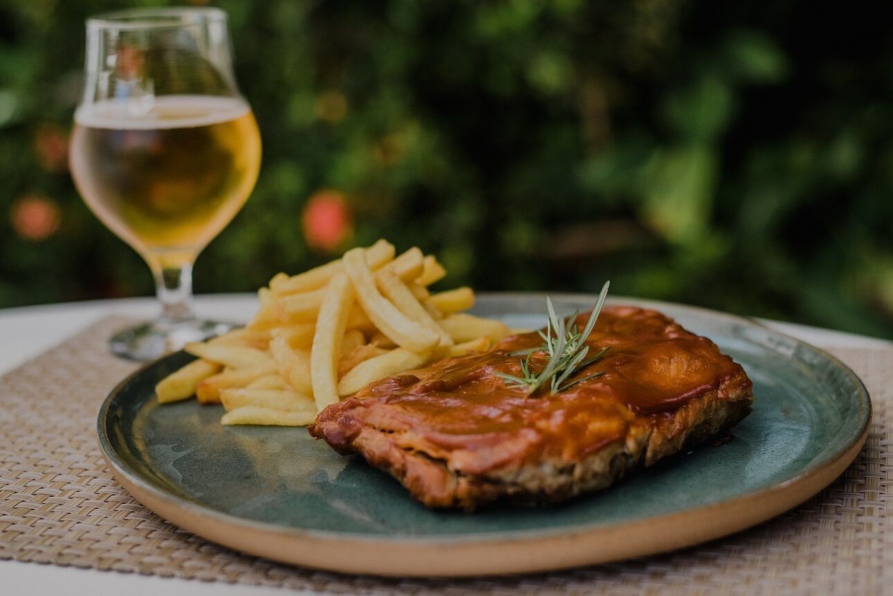 A plate with a meat dish and fries, a glass of beer, and a woven placemat.