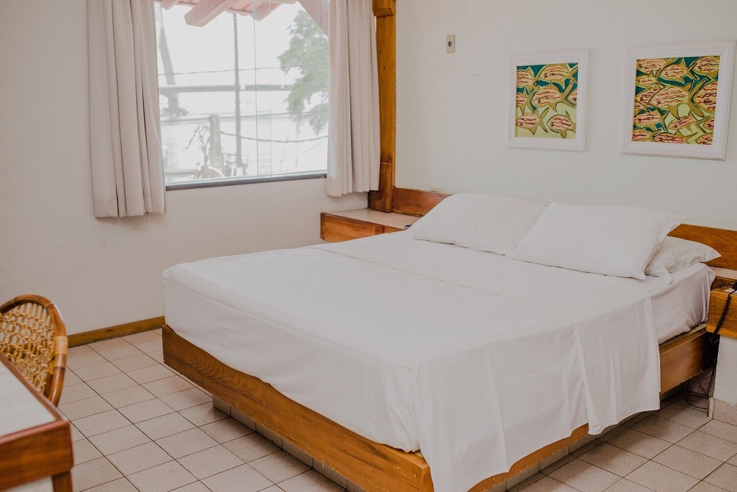 Un dormitorio limpio y bien iluminado con una cama de madera, una mesita de noche pequeña, una silla y una ventana con cortinas.