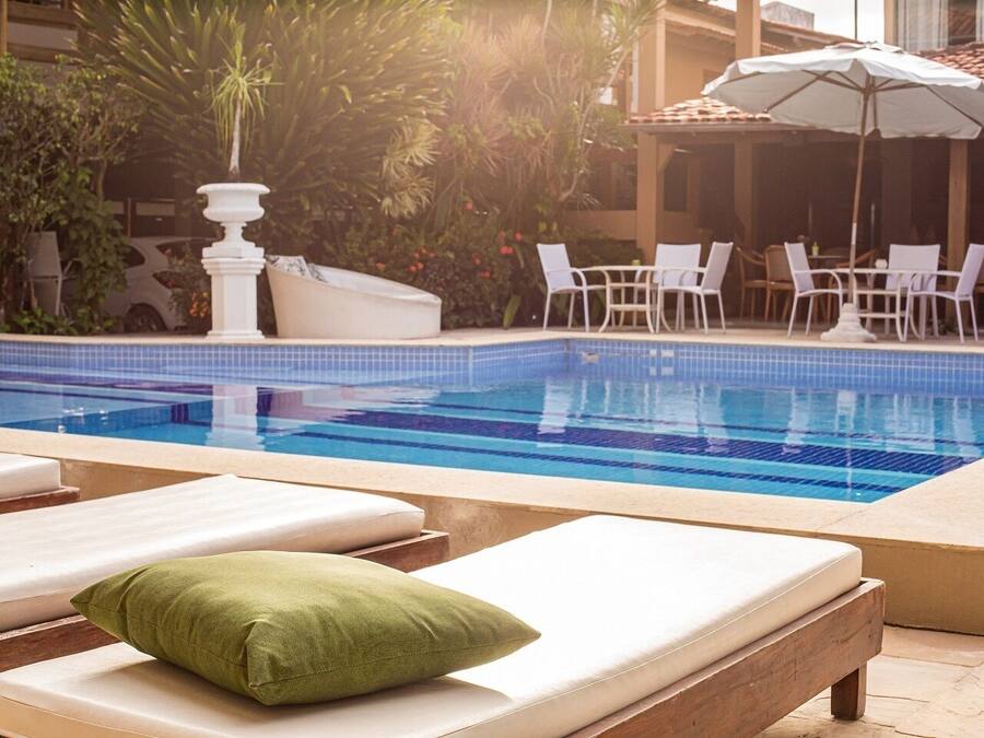 A pool area with lounge chairs and umbrellas, surrounded by greenery and a tiled pool.