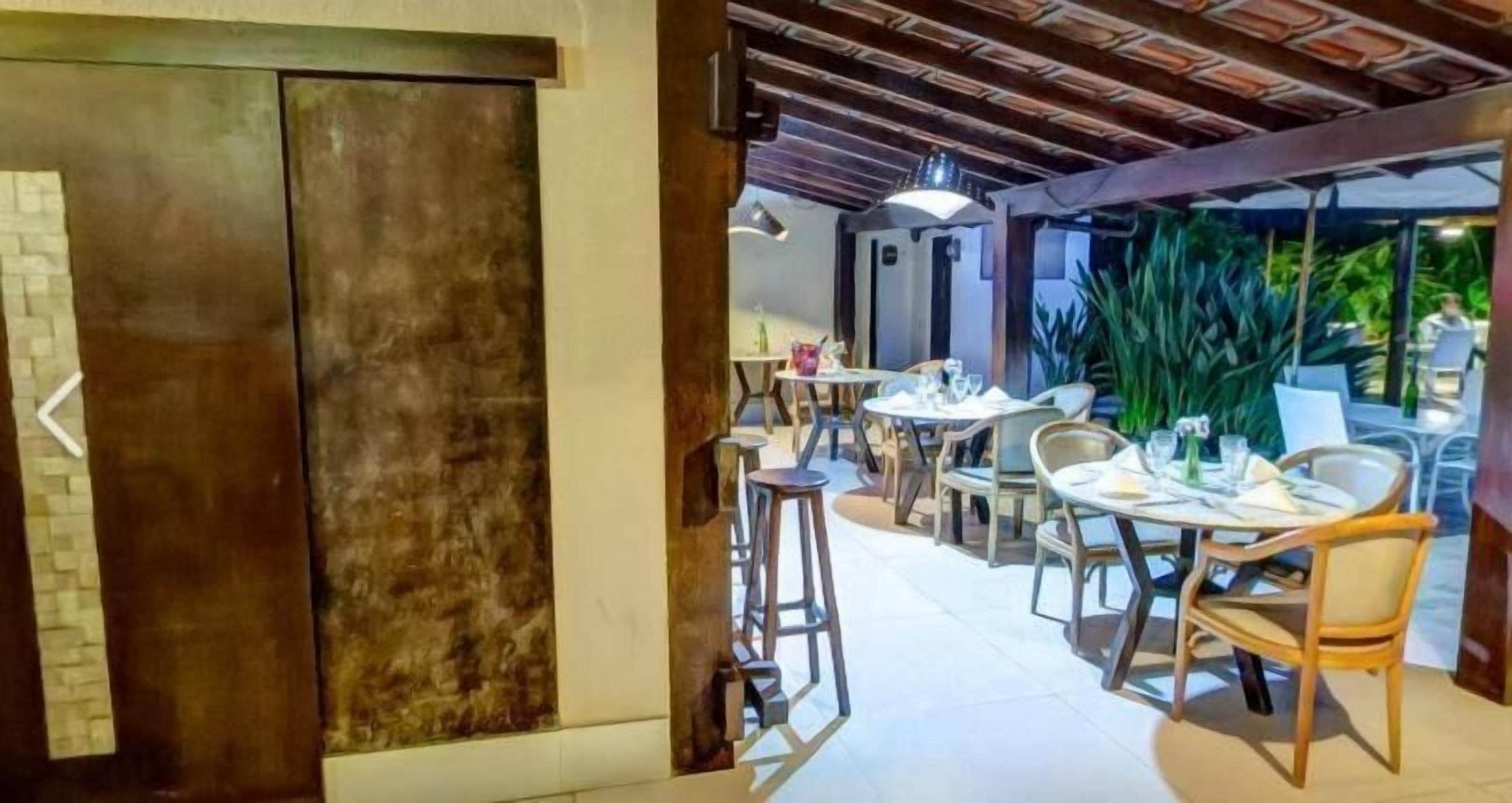 An indoor dining area with round tables and chairs, a wooden ceiling, and a view of greenery outside.
