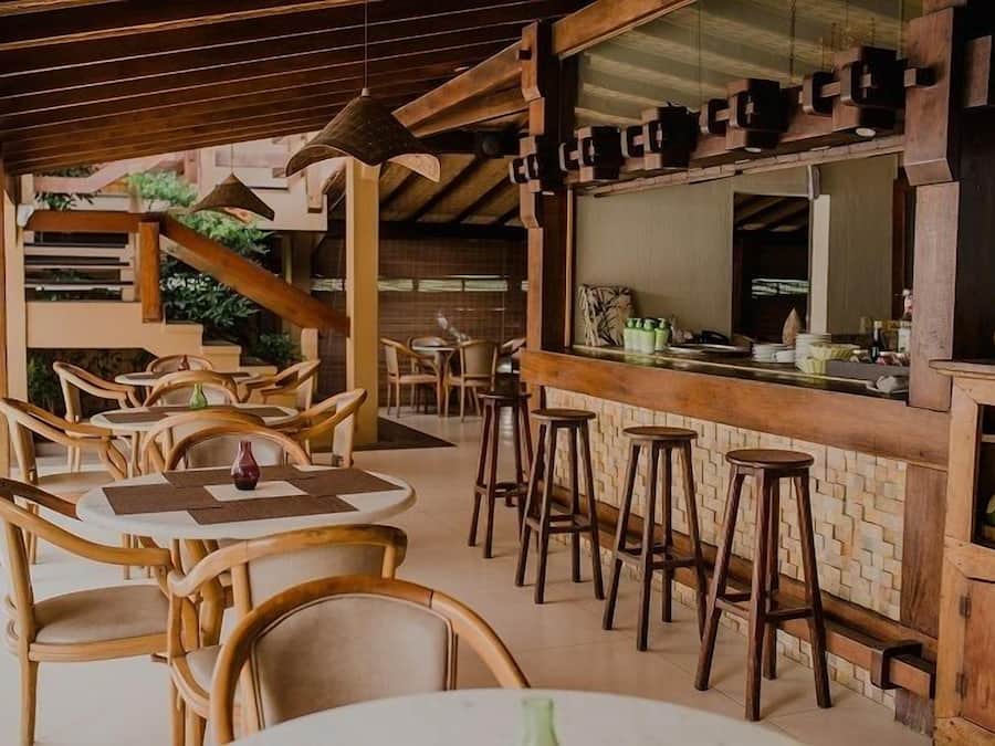 A restaurant with wooden furniture, a bar area, and a view of the outdoor garden.
