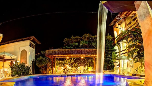 A nighttime swimming pool with a waterfall feature, surrounded by lounge chairs and a covered seating area. - Pousada Pier do Pontal (Ilhéus)