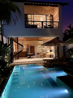 Una casa moderna de dos pisos con piscina, escalera espiral y mobiliario de exterior.