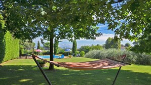 A hammock under a tree in a well-maintained garden with a pool and lounge chairs in the background. - Casa Andreini (Capannori)