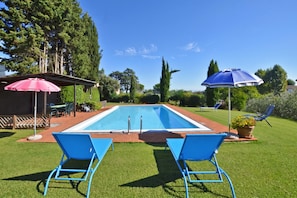 Une piscine avec deux chaises longues bleues, un parasol rose et un parasol bleu.