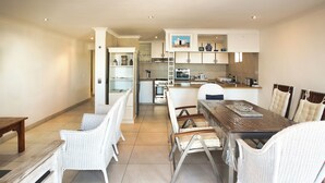 Una cocina moderna con armarios blancos, un comedor con sillas de mimbre y una mesa de madera.