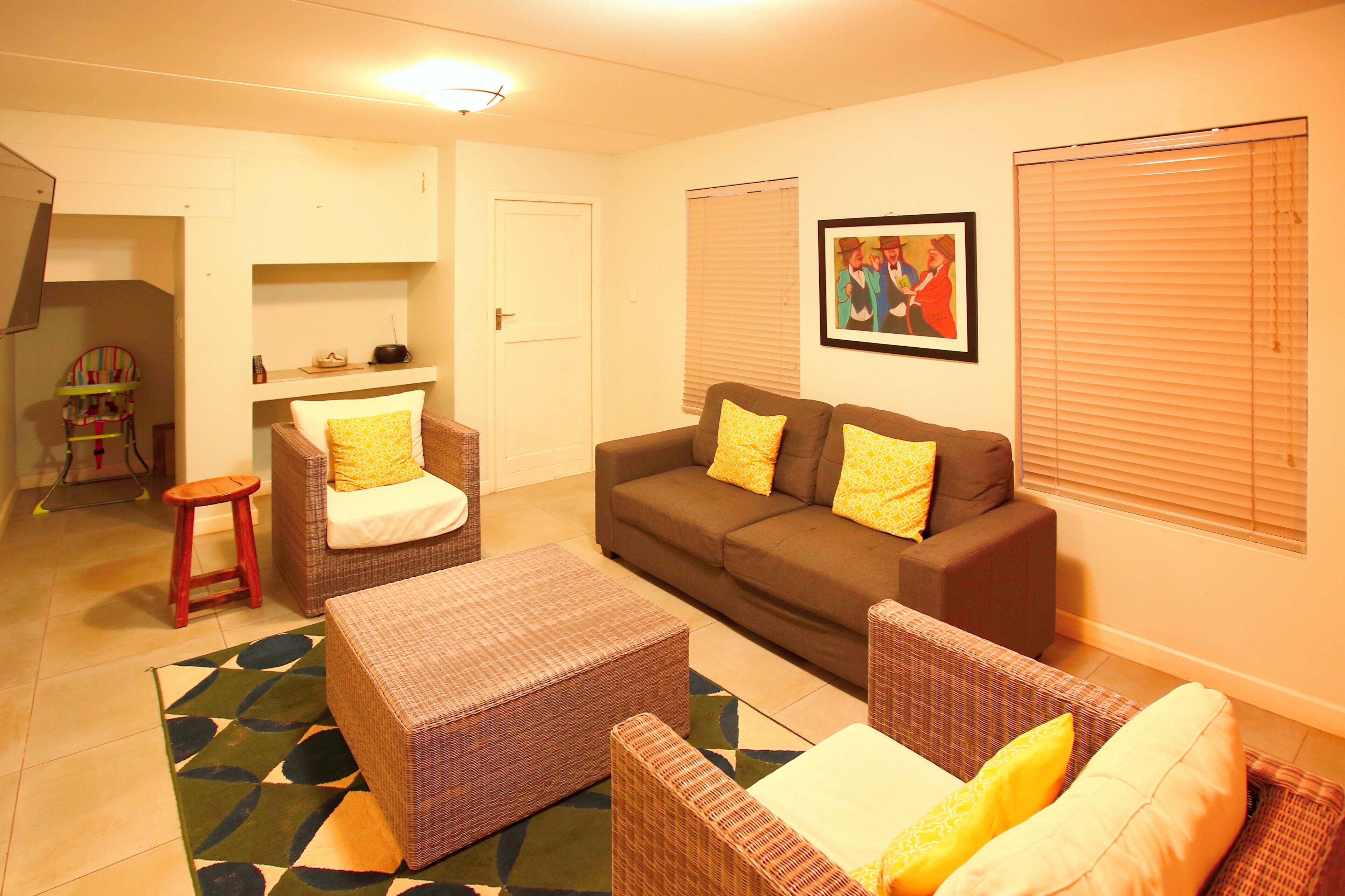 A living room with a brown sofa, two armchairs, a small table, and a colorful rug.