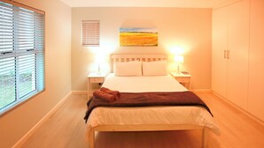 A bedroom with a bed, two bedside tables, a nightstand, a window with blinds, a painting on the wall, and a wardrobe. - 99 Steps, Langebaan 8-sleeper (Langebaan)