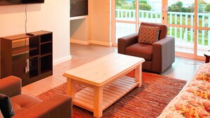 A modern living room with a flat-screen TV, a wooden coffee table, a sofa, and a large window with a view of a balcony. - 99 Steps, Langebaan 8-sleeper (Langebaan)