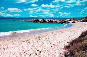 Une plage de sable fin bordée d’une eau turquoise et cristalline, parsemée de rochers.
