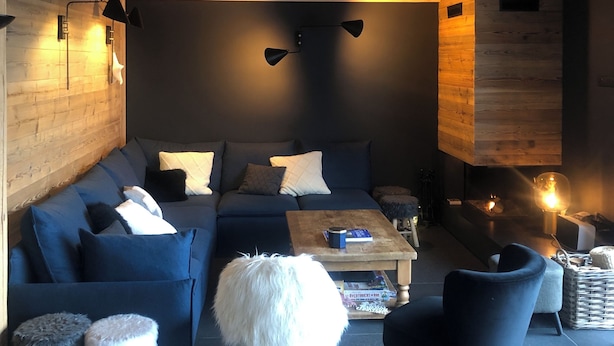 Un salon chaleureux avec un canapé bleu foncé, une table basse en bois et un pouf blanc moelleux.