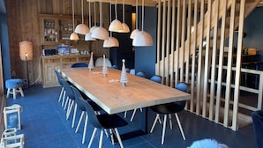 Un espace de salle à manger moderne avec une table en bois, des chaises noires et des luminaires suspendus.