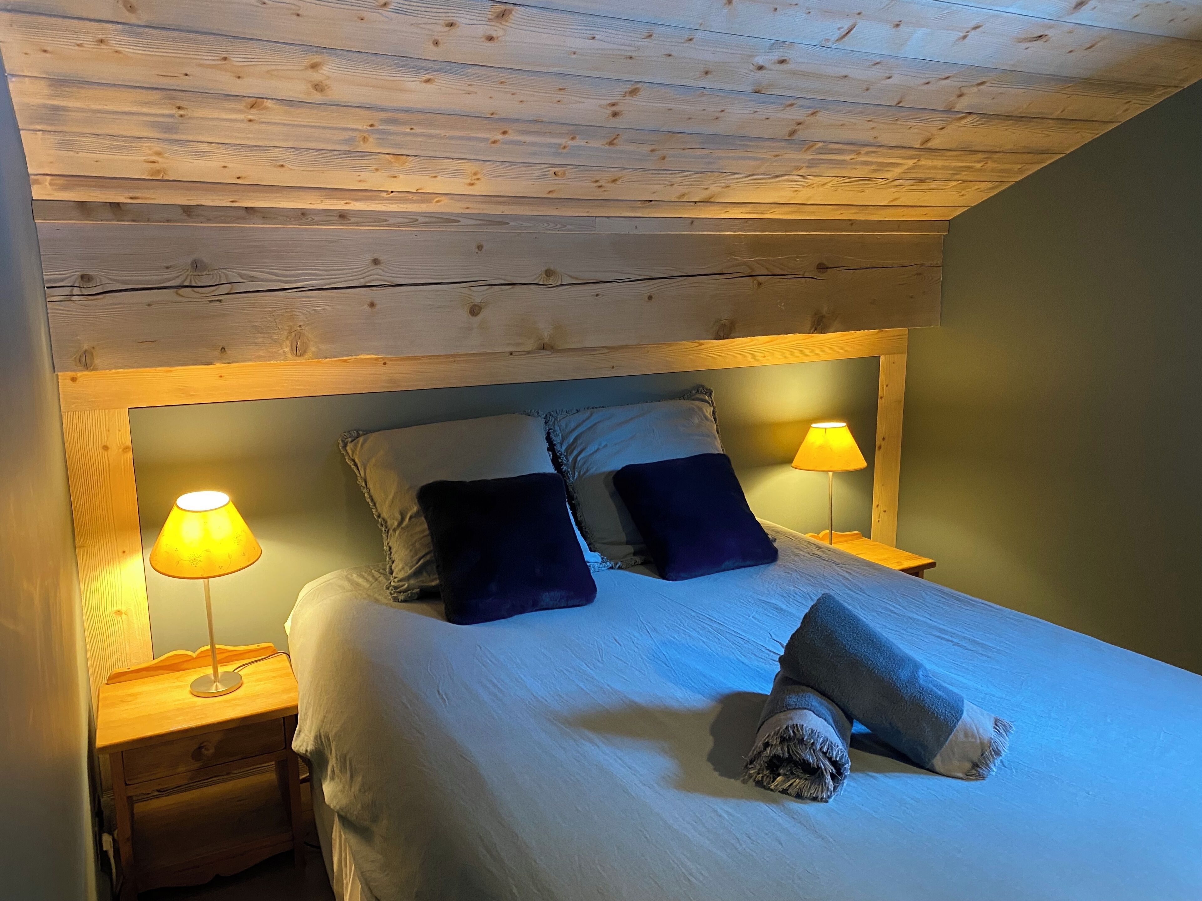 A wooden ceiling, a bed with pillows, and two bedside lamps.