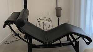 Una habitación moderna con una butaca reclinable, una mesita hexagonal pequeña con dos vasos, una lámpara negra alta y una lámpara de pie.