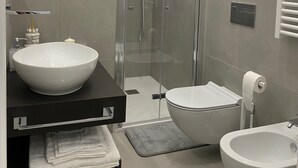 Un baño moderno con ducha de vidrio, lavamanos blanco, inodoro y bidé.