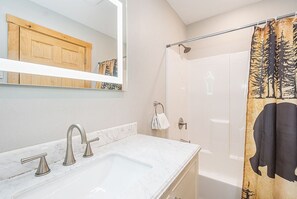 A bathroom with a marble sink, a shower with a curtain, and a wooden cabinet above the mirror. - All about the view  (McHenry)