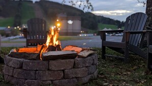 A campfire in a stone fire pit with Adirondack chairs nearby.