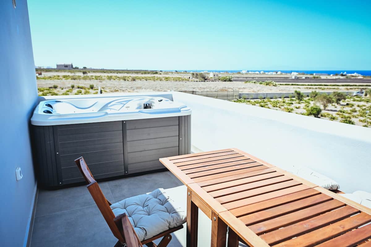 A wooden table and a cushioned chair on a balcony with a hot tub and a view of the beach.