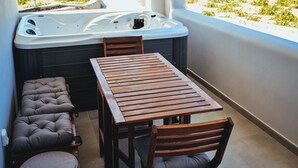 Uma varanda com mesa e cadeiras de madeira, um banco acolchoado e uma banheira de hidromassagem.