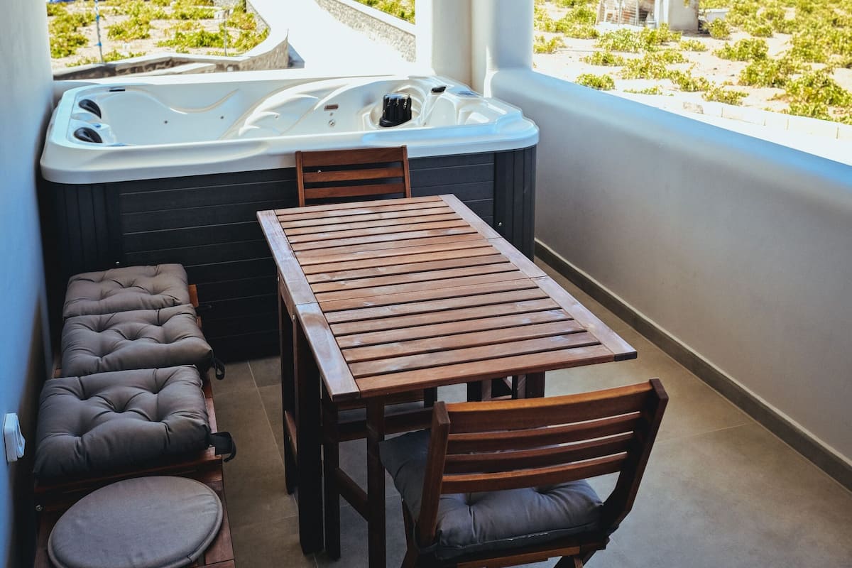 A balcony with a wooden table and chairs, a cushioned bench, and a hot tub.