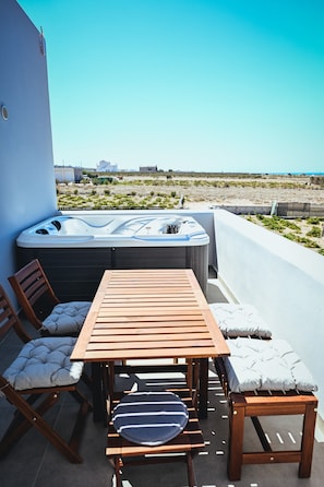 A rooftop terrace with a wooden table and chairs, a hot tub, and a view of the beach. - Abelonas Houses (Santorini)