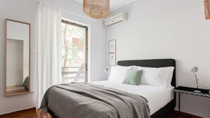 Un dormitorio con cama, mesita de noche con lámpara, espejo y ventana con cortinas.