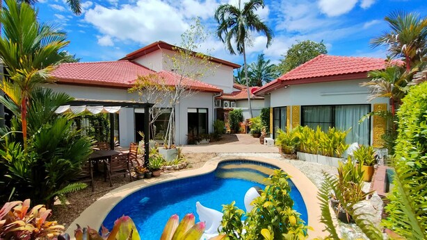Um imóvel residencial com piscina, varanda coberta e diversas plantas tropicais.