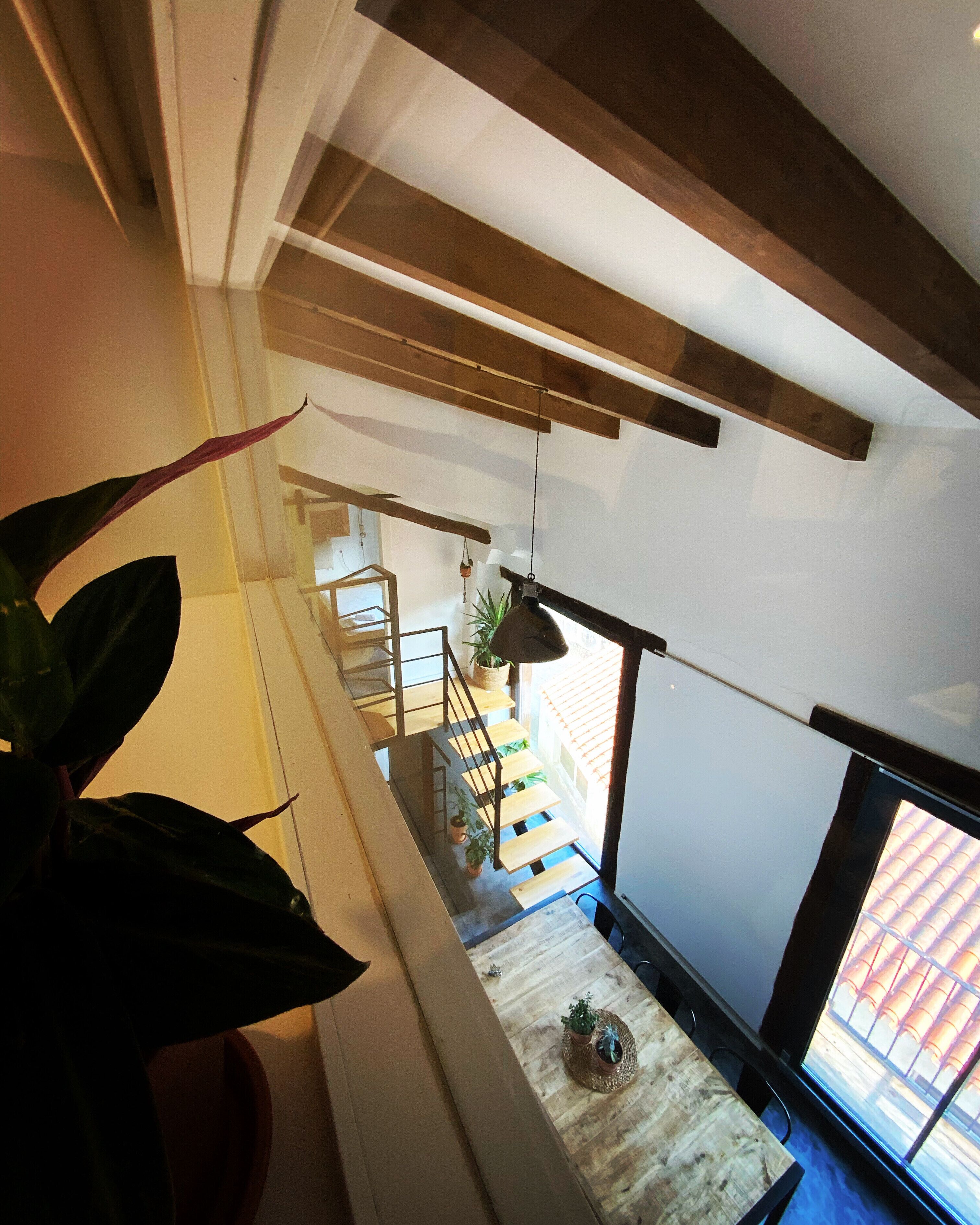 Un intérieur moderne avec un escalier en bois, un coin repas comprenant une table et des chaises, et une vue sur l’extérieur grâce à une grande fenêtre.