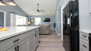 A modern kitchen with a large island, a black refrigerator, and a ceiling fan. - Seneca Spirit: Gorgeous Views of Seneca Lake! (Geneva)