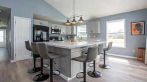 A modern kitchen with a central island, bar stools, and a large window providing natural light. - Seneca Spirit: Gorgeous Views of Seneca Lake! (Geneva)