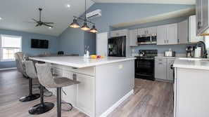 A modern kitchen with a large island, bar stools, a ceiling fan, and a flat-screen TV. - Seneca Spirit: Gorgeous Views of Seneca Lake! (Geneva)