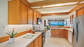 Een moderne keuken met houten kastjes, een roestvrijstalen koelkast en uitzicht op zee.
