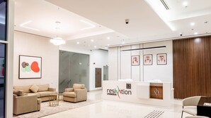 A modern reception area with a reception desk labeled "resivation," a sofa, chairs, and a glass wall. - Resivation Hotel (Dubai)