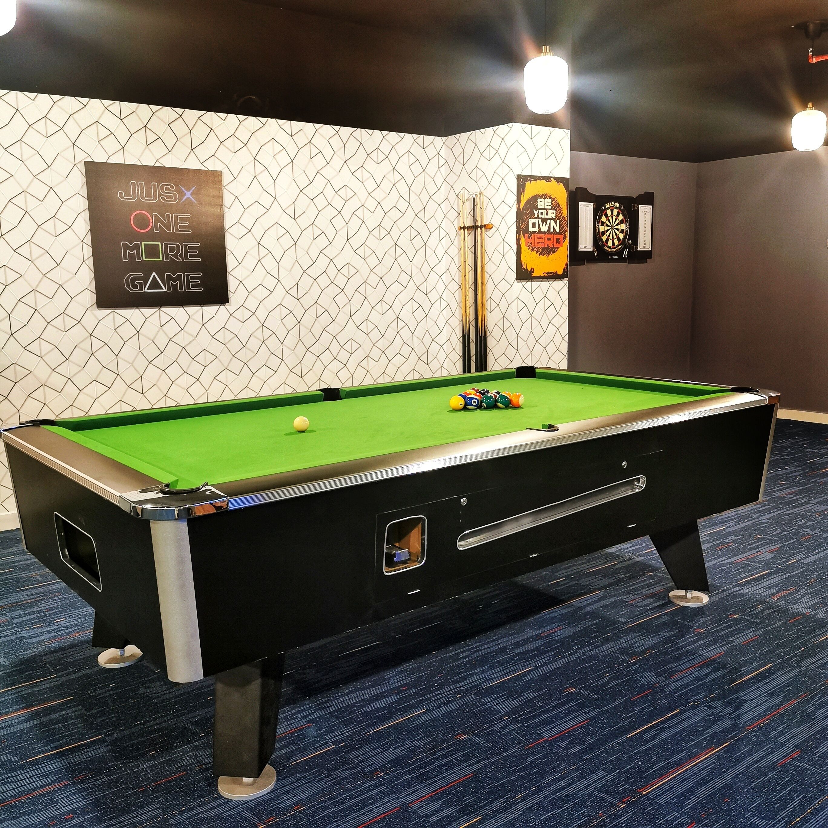 A pool table with balls, a dartboard, and a sign that reads "JUSX ONE MORE GAME".