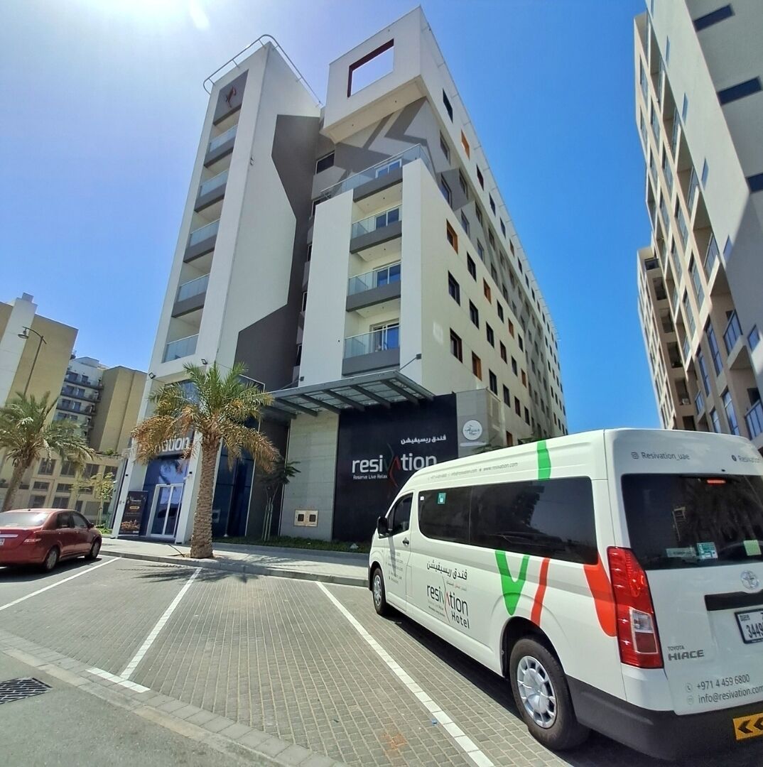 A modern hotel building with a prominent 'Resi' sign, a white van parked in front, and palm trees lining the street.