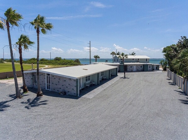 Een motel aan het strand met een overdekte parkeerplaats, palmbomen en uitzicht op de oceaan.