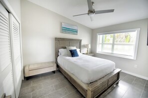 A bedroom with a bed, a bench, a ceiling fan, a window, and a wall-mounted lamp. - Flip Flops and Bikini Tops #1 - Direct River Access (Cocoa Beach)