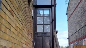 A narrow stairway leading to a dark wooden door with a small window, flanked by brick walls and a metal handrail.