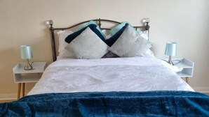 A neatly made bed with a white and blue duvet, two pillows, and a dark blue blanket. There are two bedside tables with lamps.