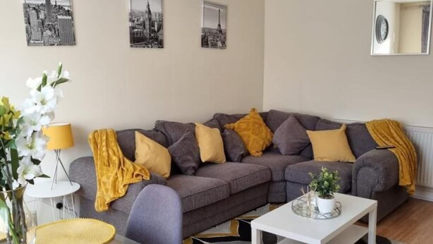 A modern living room with a grey sofa, yellow cushions, a glass coffee table, and a patterned rug.