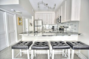 A modern kitchen with white cabinetry, a marble island, and a stainless steel refrigerator. - Sandals and Scandals #2- Direct River Access and Beach (Cocoa Beach)