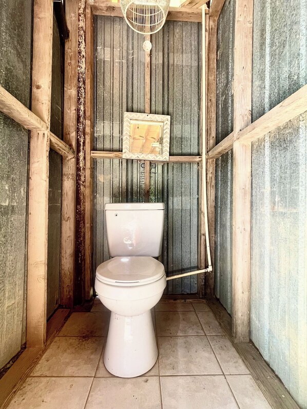 Un baño pequeño y rústico con inodoro, paredes de madera y techo de lámina corrugada.