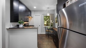 Une cuisine moderne avec des meubles de couleur sombre, un réfrigérateur en acier inoxydable et un petit îlot central agrémenté d’une plante.